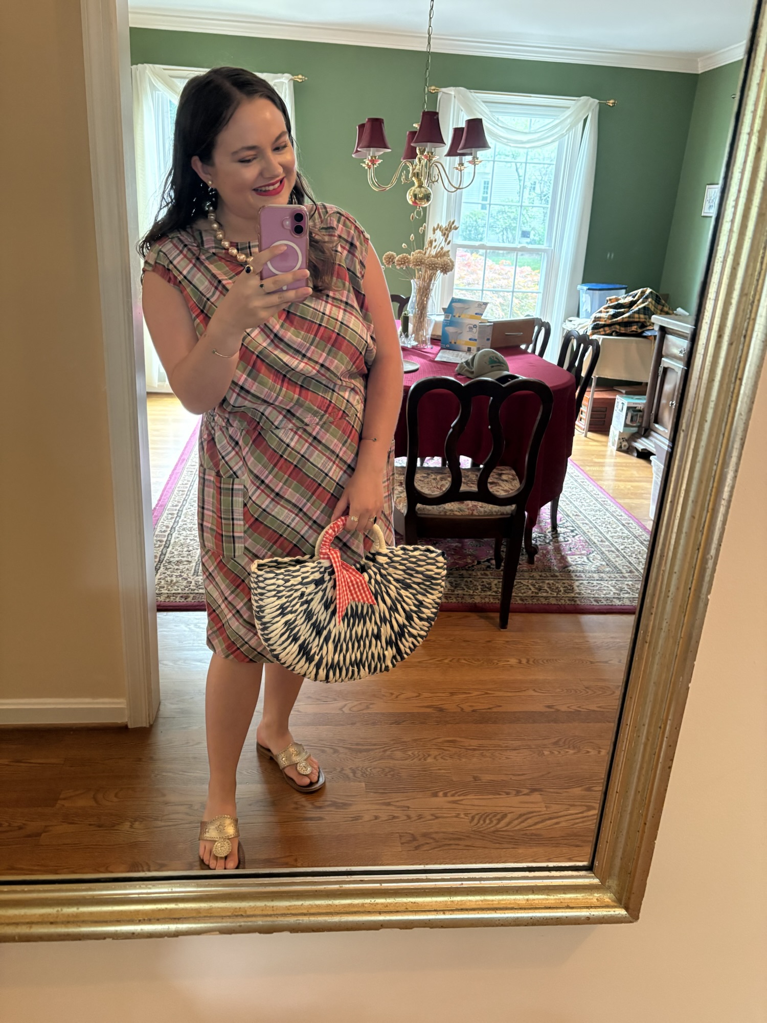 pink chickadee wearing a pink and red checkered plaid midi dress, metallic gold slide sandals, and holding a graphic black and white woven chevron straw handbag
